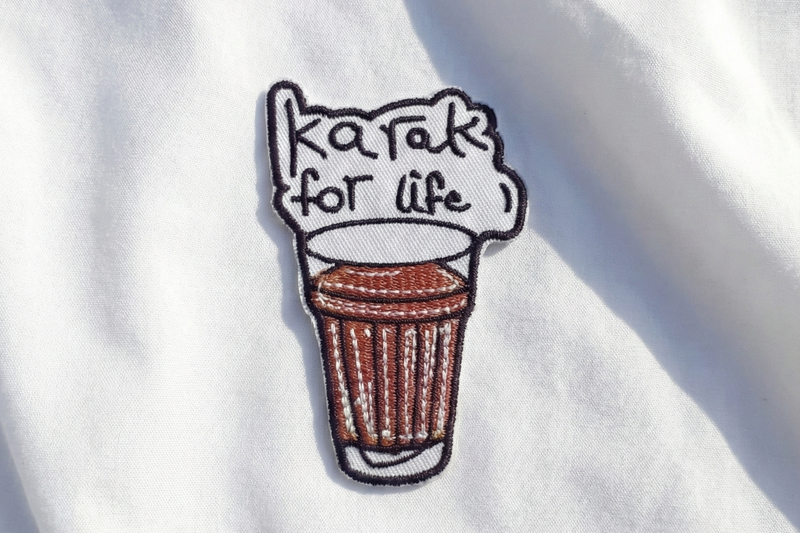 Embroidered patch of a coffee cup with 'karaok for life' text on white fabric.